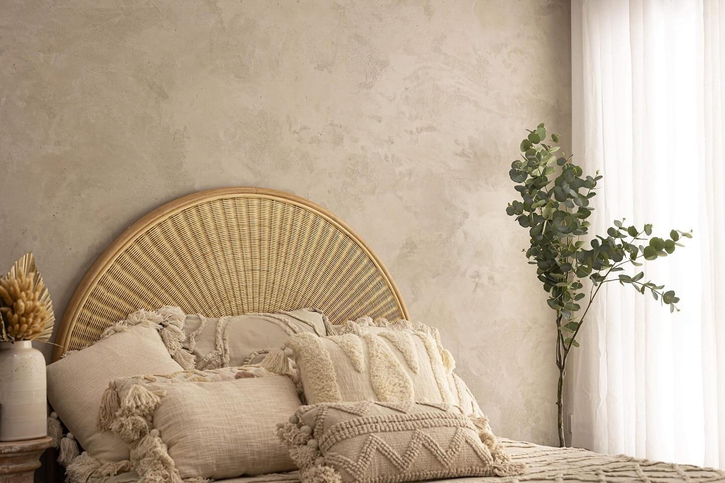 Bedroom with a textured beige plaster feature wall behind a rattan bedhead