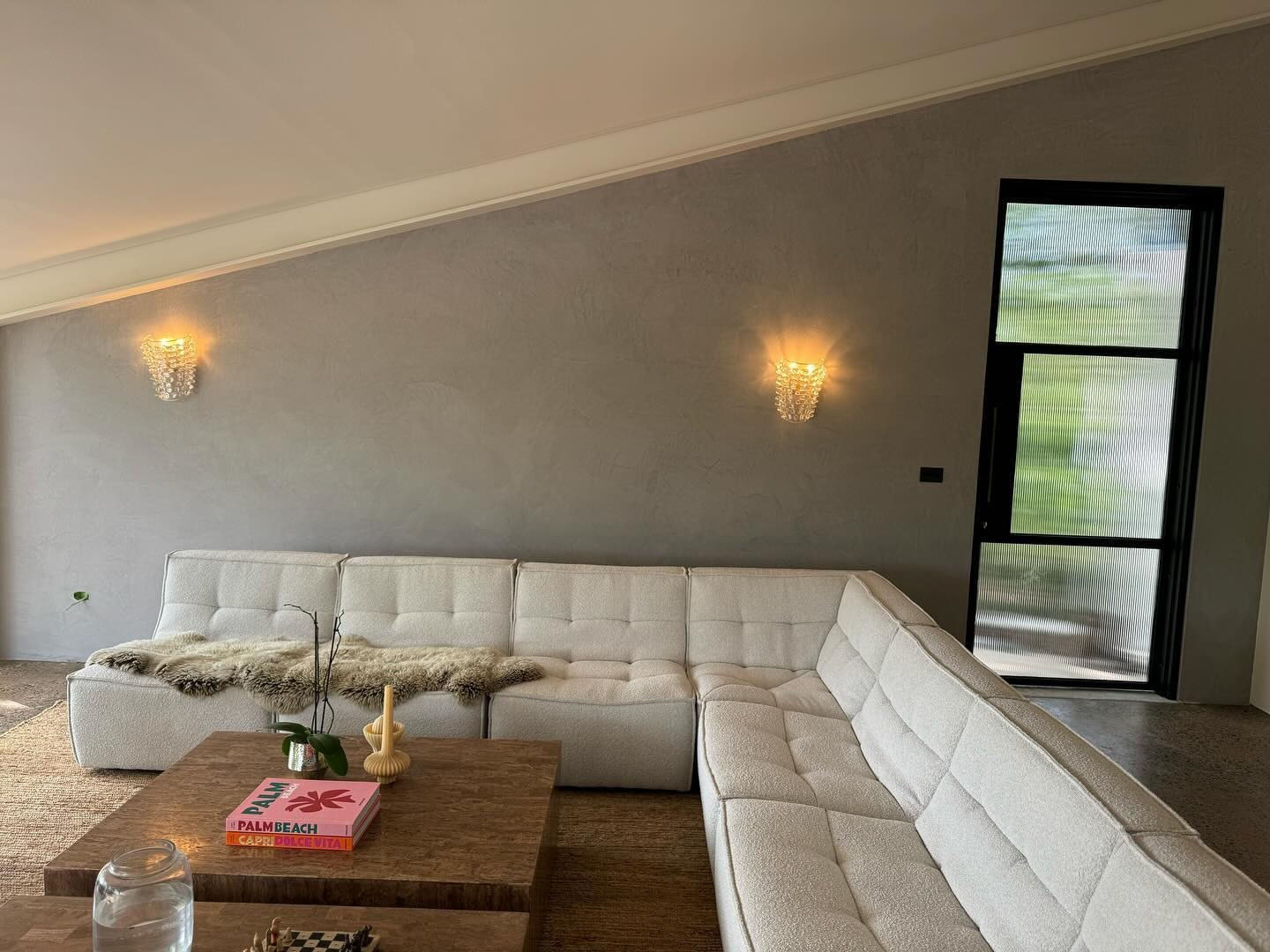 Living room with a grey plaster feature wall, wall lights and a white modular sofa