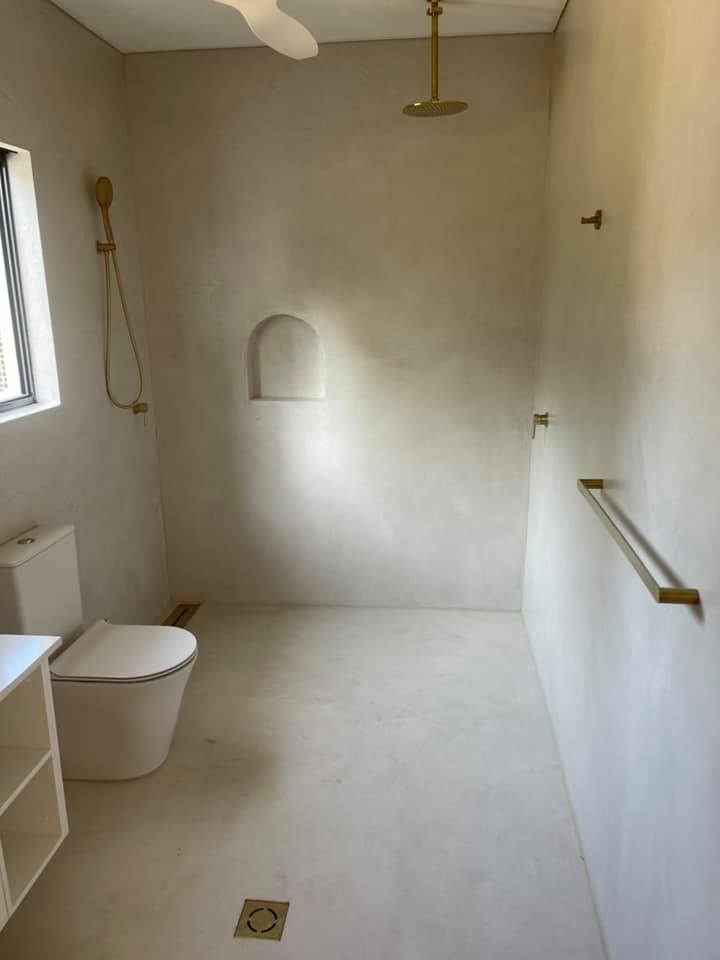 Walk-in shower with seamless beige walls and floor, a brass towel rail and wall niche