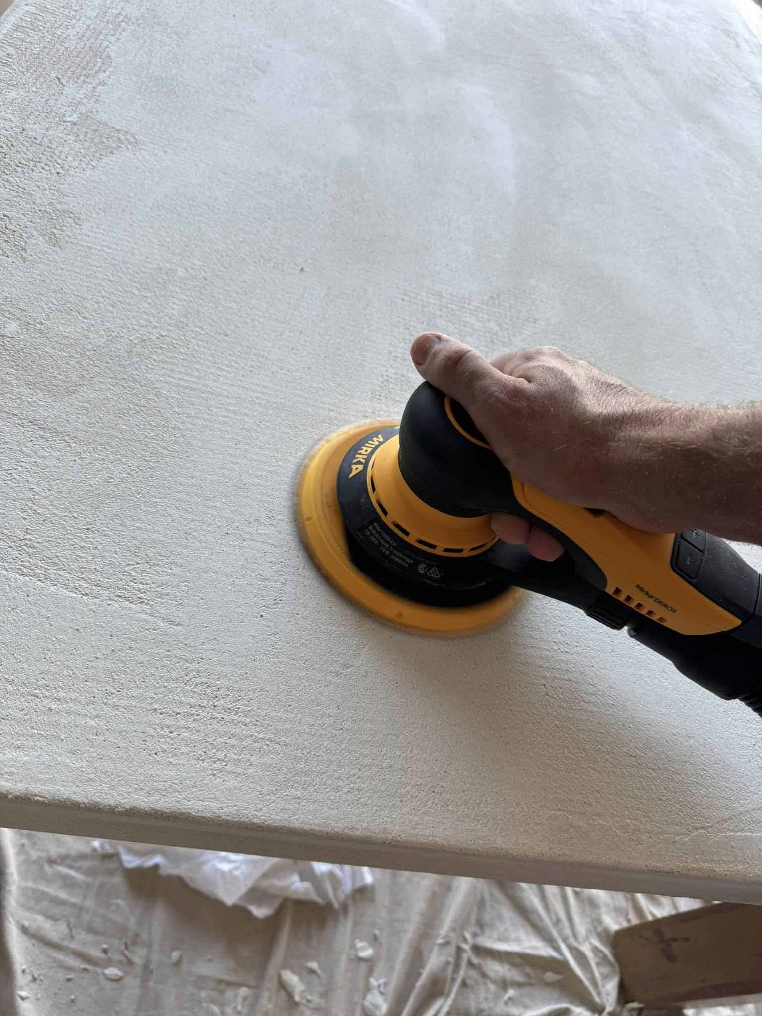 Hand using an orbital sander on a freshly coated white surface