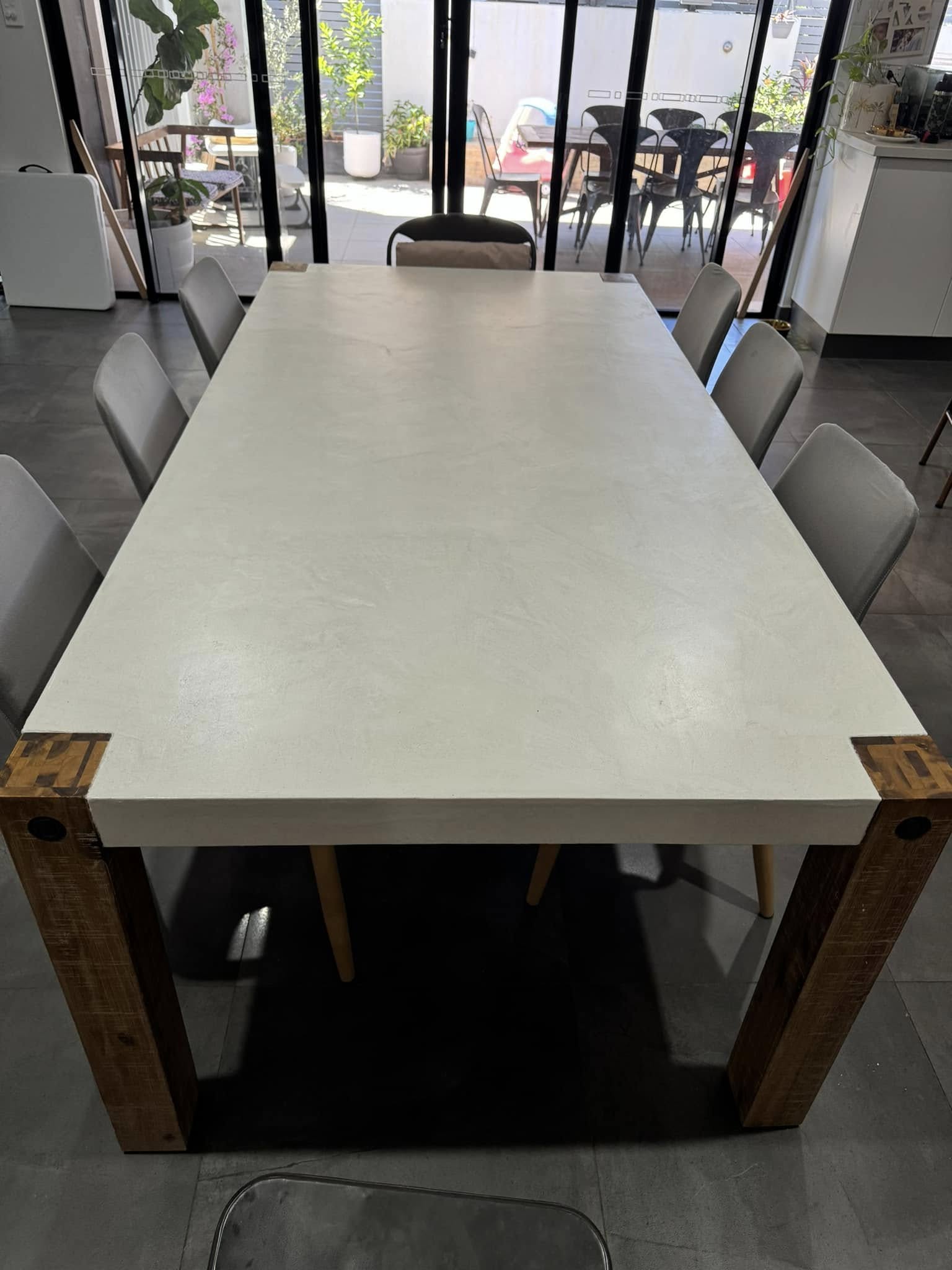 Long dining table with a smooth white concrete-look top and timber legs
