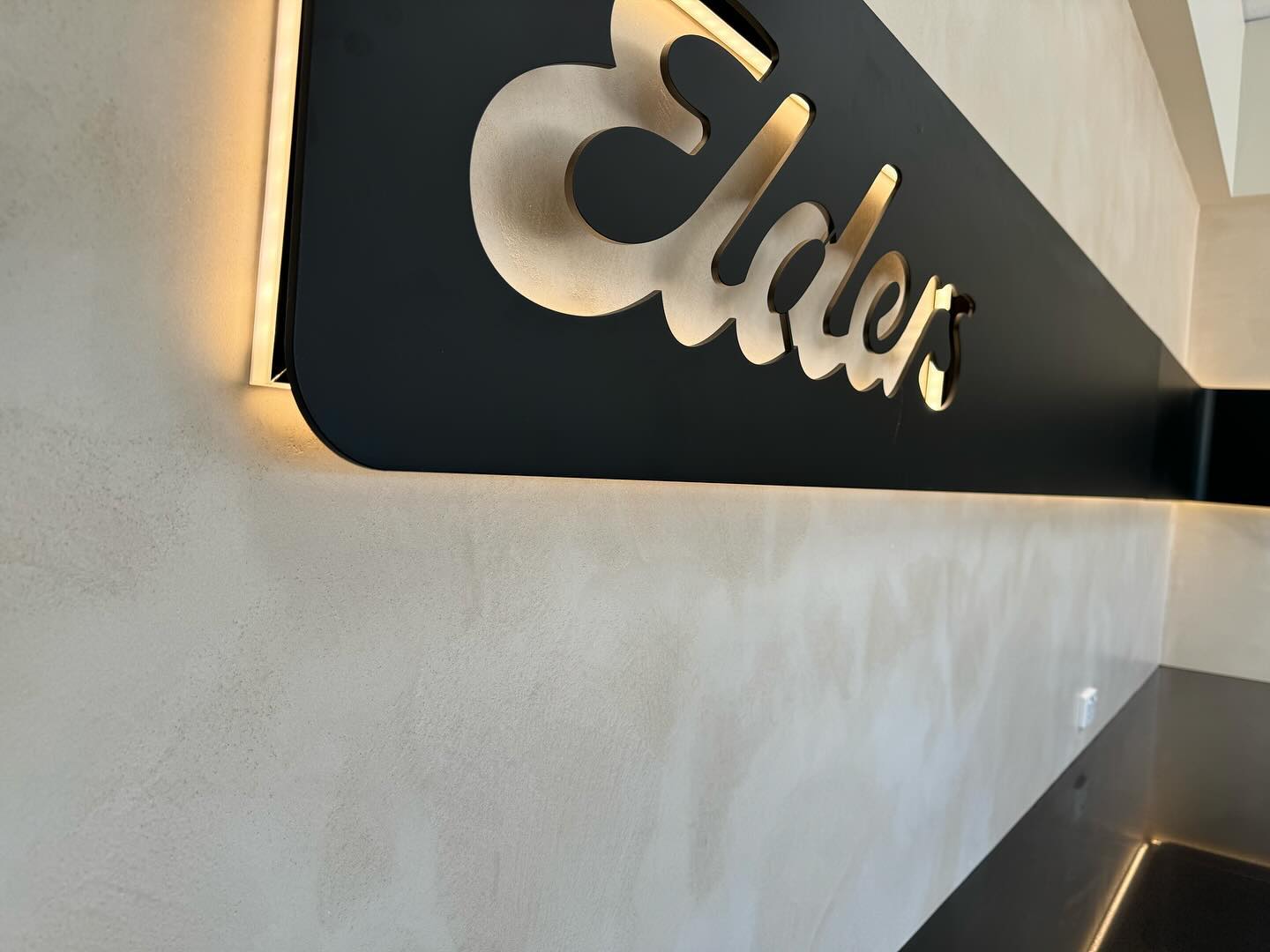 Illuminated Elders sign mounted on a smooth pale wall
