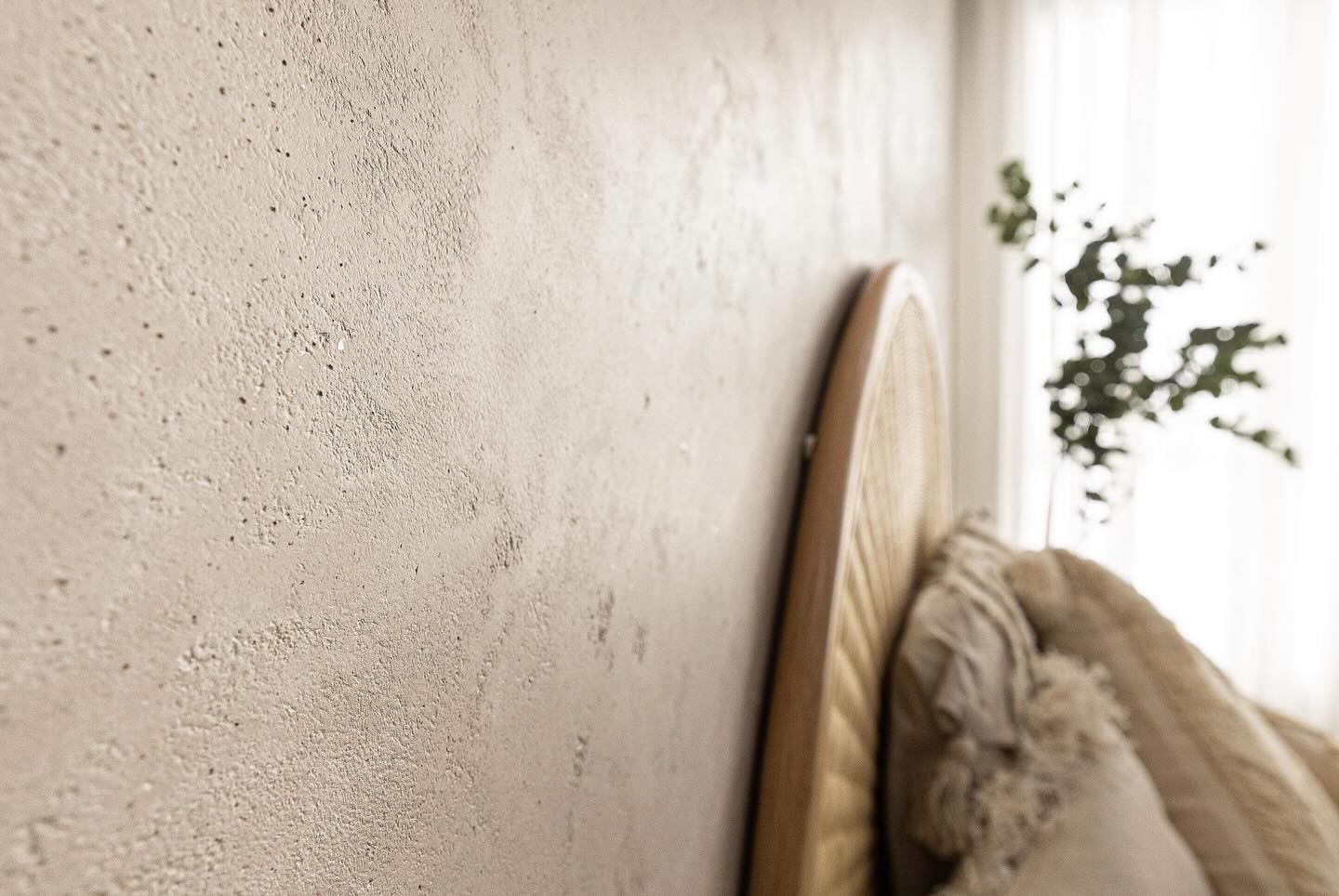 Close-up of a textured beige plaster wall beside a rattan bedhead