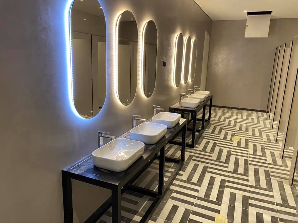 Bathroom with grey plaster walls, backlit oval mirrors and a row of basins