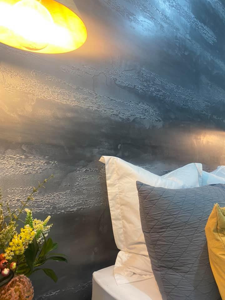 Close-up of a dark grey metallic plaster wall lit by a pendant lamp above a bed
