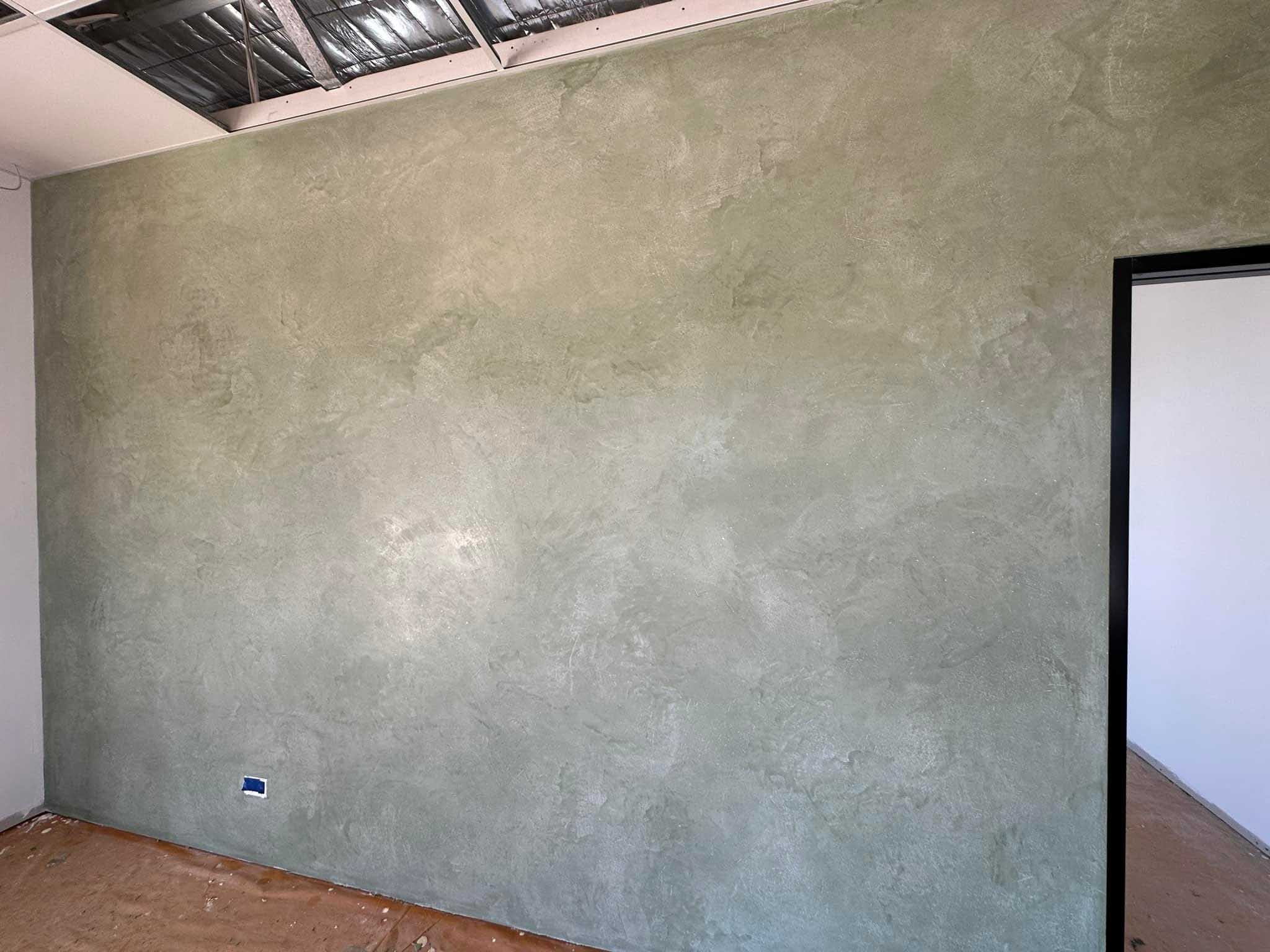 Room with a sage green mottled plaster feature wall and an open ceiling