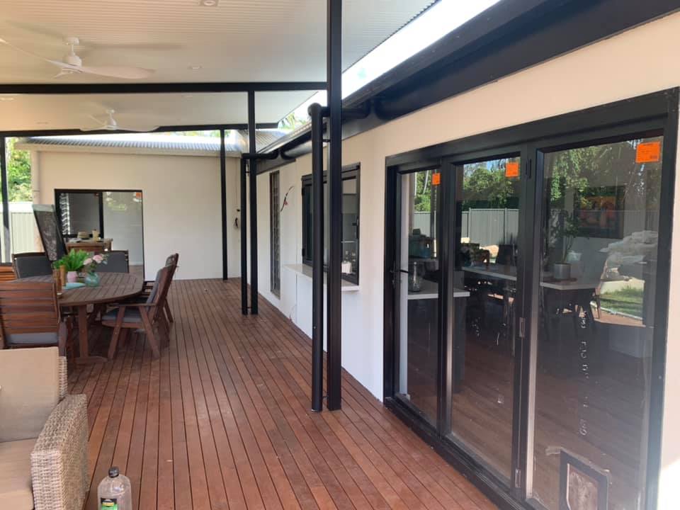 Covered timber deck beside a white rendered wall and glass sliding doors