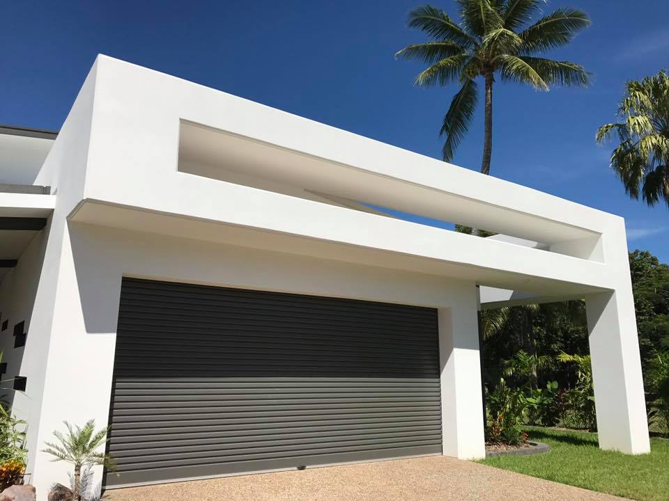 White rendered garage frame with a dark roller door and palm trees