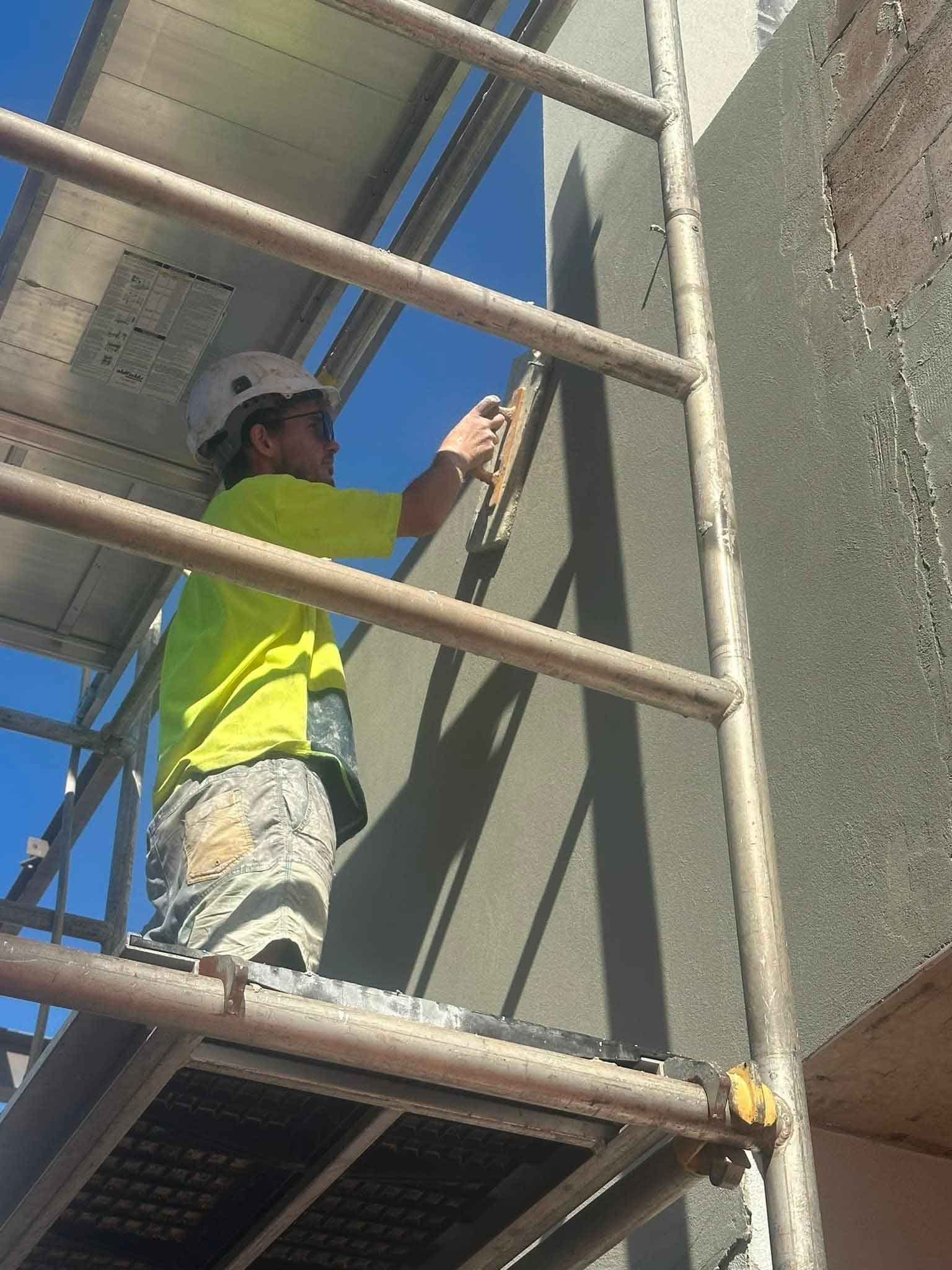 Worker in hi-vis on scaffolding working on an exterior rendered wall