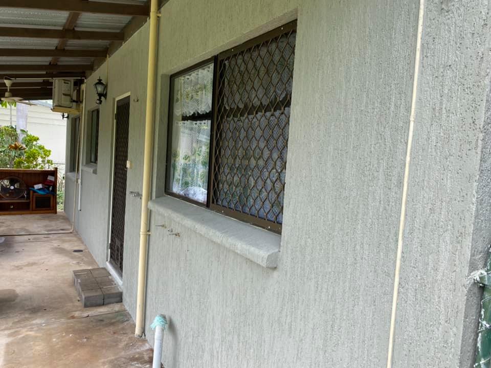 Grey textured rendered house wall with a security-screened window