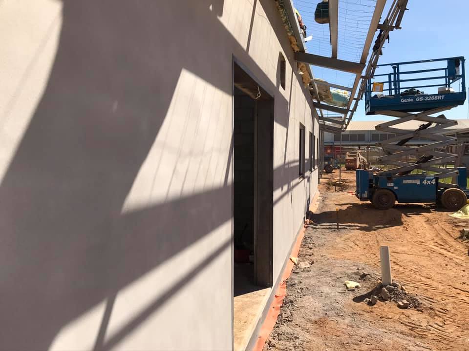 Long rendered building wall on a construction site with a scissor lift
