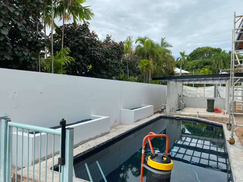 White rendered pool fence wall and planter boxes beside a swimming pool