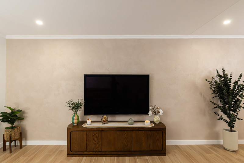 Living room with a beige plaster feature wall behind a TV and timber cabinet