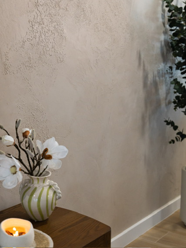 Textured beige plaster wall behind a striped vase of white flowers and a candle