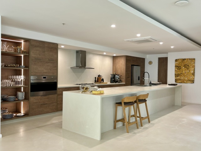 Open-plan kitchen with a white waterfall island, timber cabinetry and bar stools