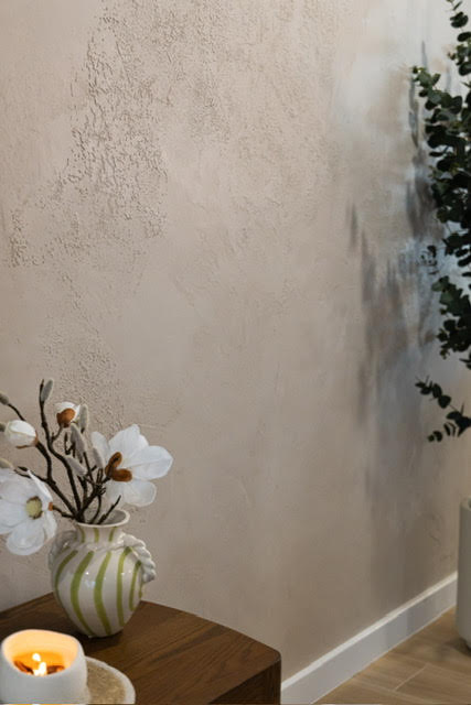 Textured beige plaster wall above a timber side table with a vase and candle